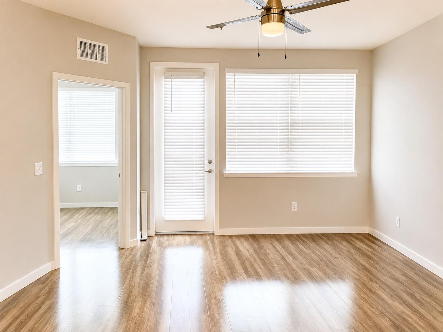 Empty, freshly cleaned living room with shining wood floors, clean blinds, and a dusted ceiling fan
