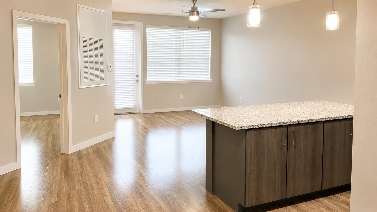 Empty, freshly cleaned open living area with gleaming wood floors and a granite kitchen island, ready for new occupants