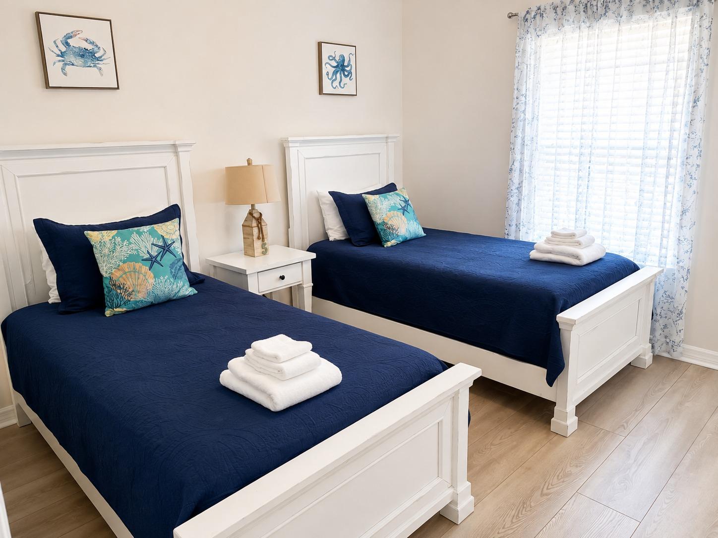 Guest-ready twin bedroom with made beds, coastal throw pillows, and folded fresh towels